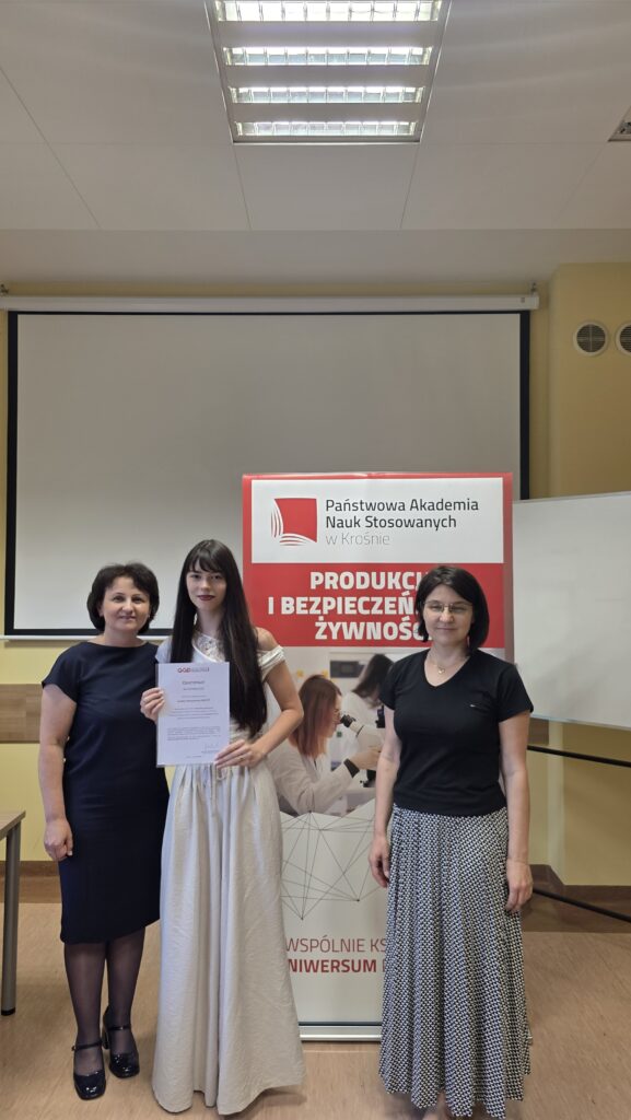 Studentka z certyfikatem stoi obok baneru kierunku Produkcja i bezpieczeństwo żywności po prawej stoi dr Dykiel, po lewej prof. Krochmal-Marczak