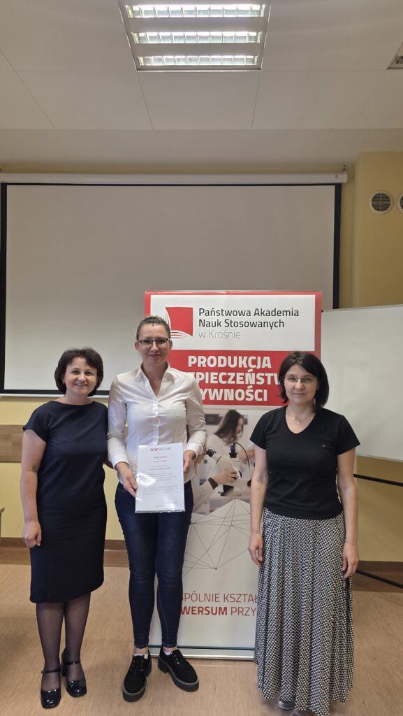 Studentka z certyfikatem stoi obok baneru kierunku Produkcja i bezpieczeństwo żywności po prawej stoi dr Dykiel, po lewej prof. Krochmal-Marczak