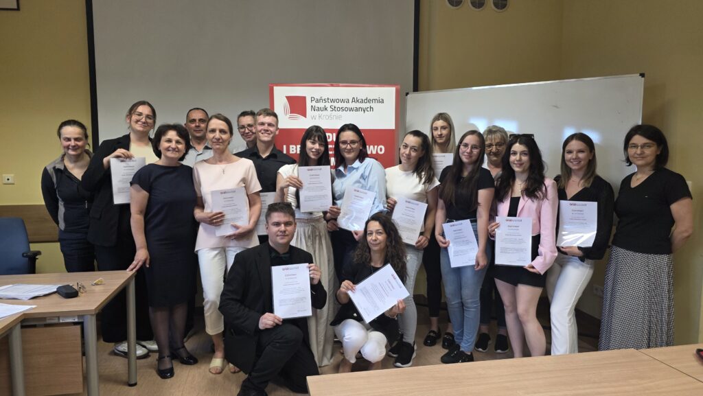 grupa wszystkich studentów z certyfikatami z tyłu biała tablica i ekran do rzutnika, poster kierunku.
