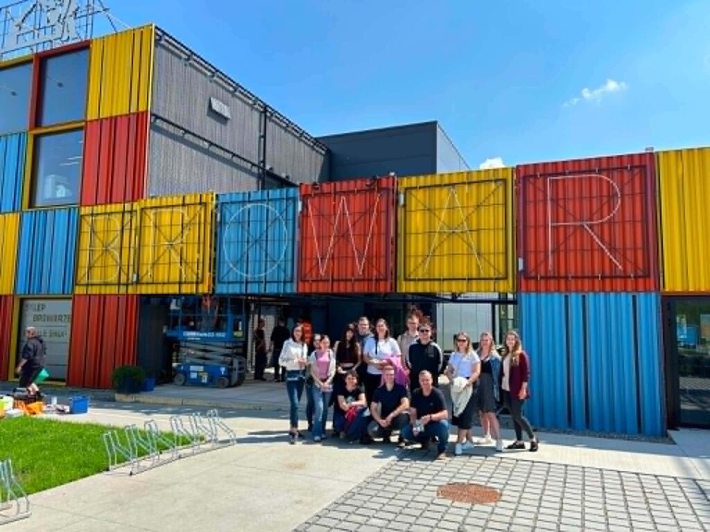 Grupa studentów na tle kontenerów kolorowych z neonem nazwy browar