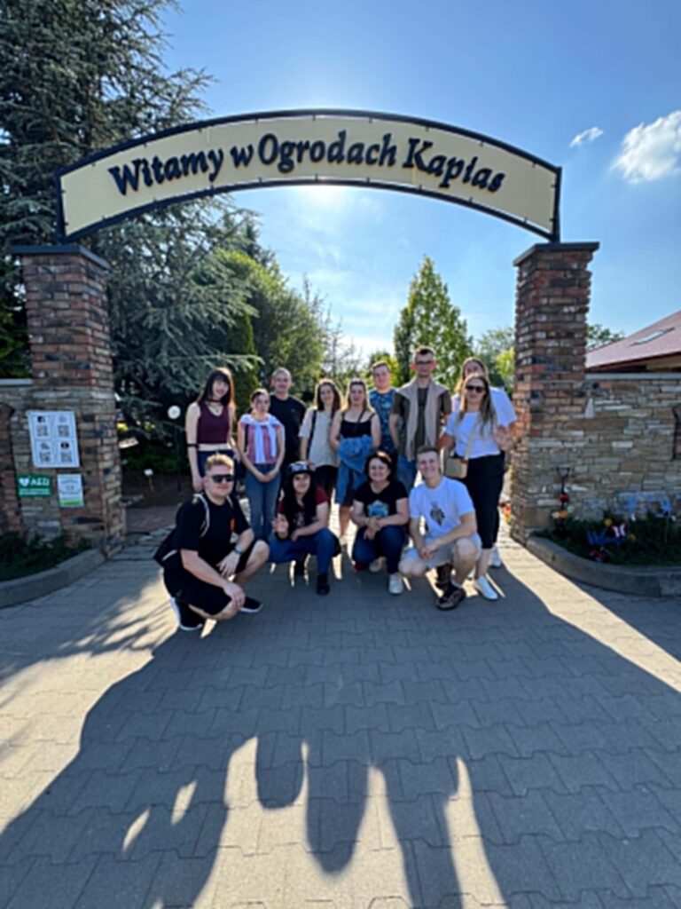 Grupa studentów na tle wejścia do ogrodów Kapias, szyld nad głowami
