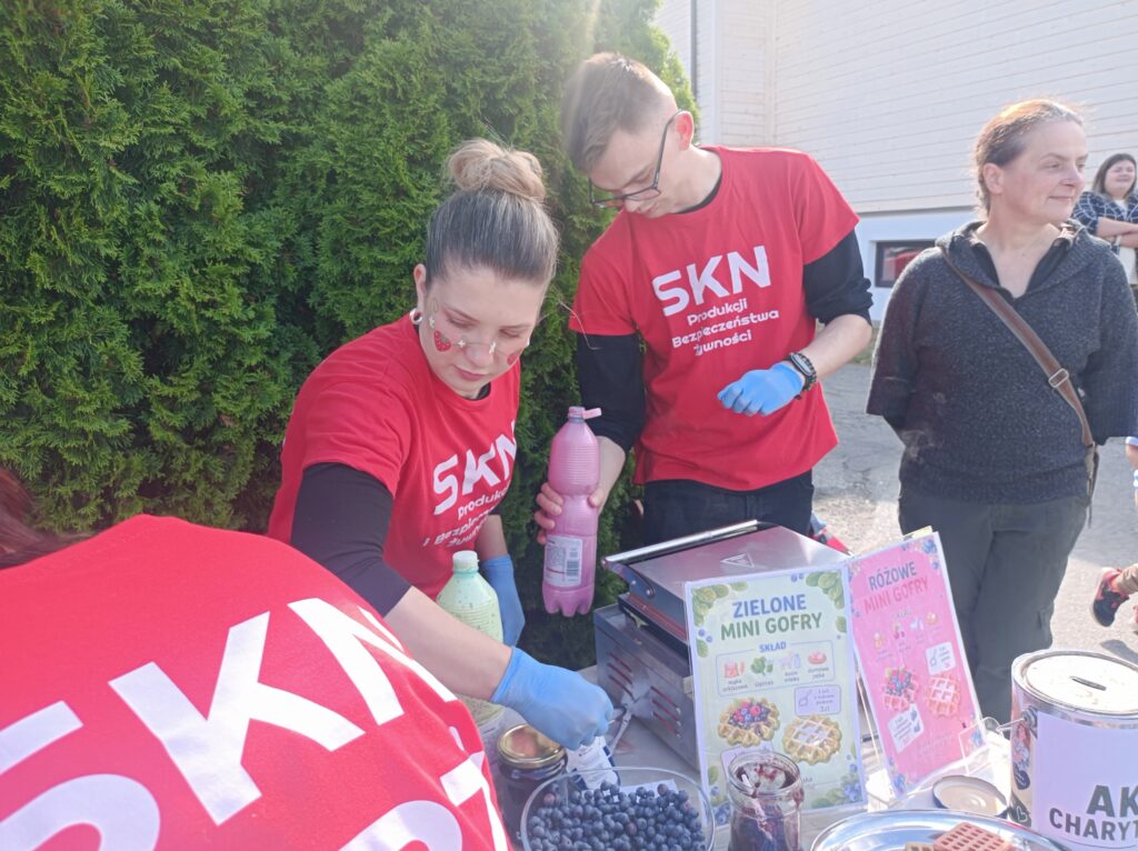 Stoisko studentów, studenci w czerwonych koszulkach z napisem SKN PIBŻ stoją i przygotowują produkty. 
