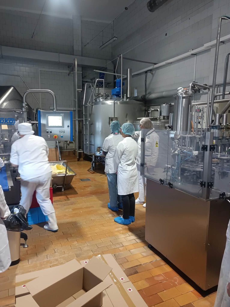 Studenci w strojach białych ochronnych w hali produkcyjnej wokół urządzenia ze stali do produkcji i przetwórstwa mleka
