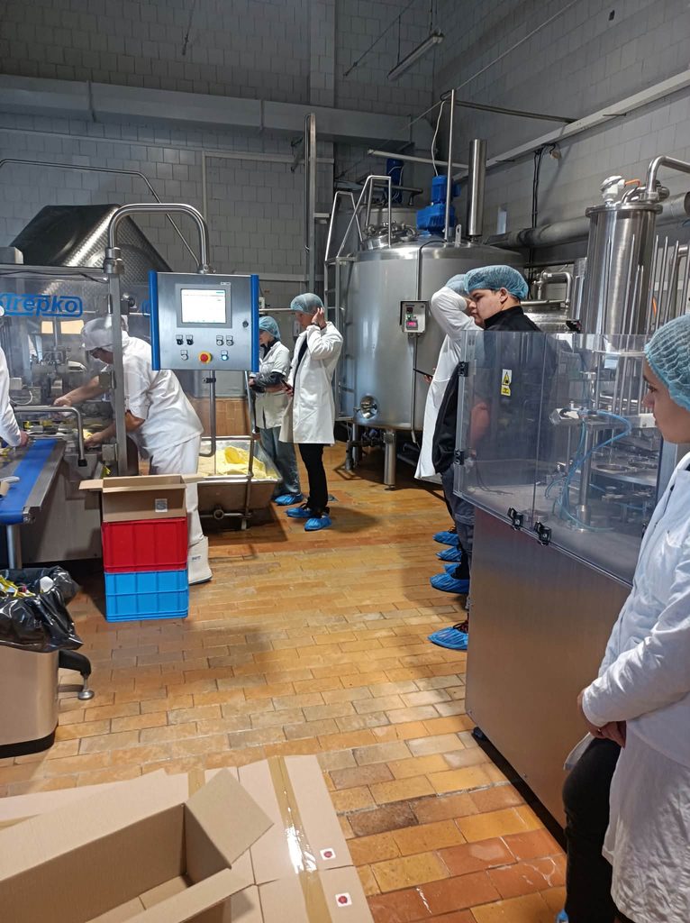 Studenci w strojach białych ochronnych w hali produkcyjnej wokół urządzenia ze stali do produkcji i przetwórstwa mleka