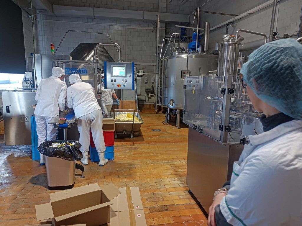 Studenci w strojach białych ochronnych w hali produkcyjnej wokół urządzenia ze stali do produkcji i przetwórstwa mleka
