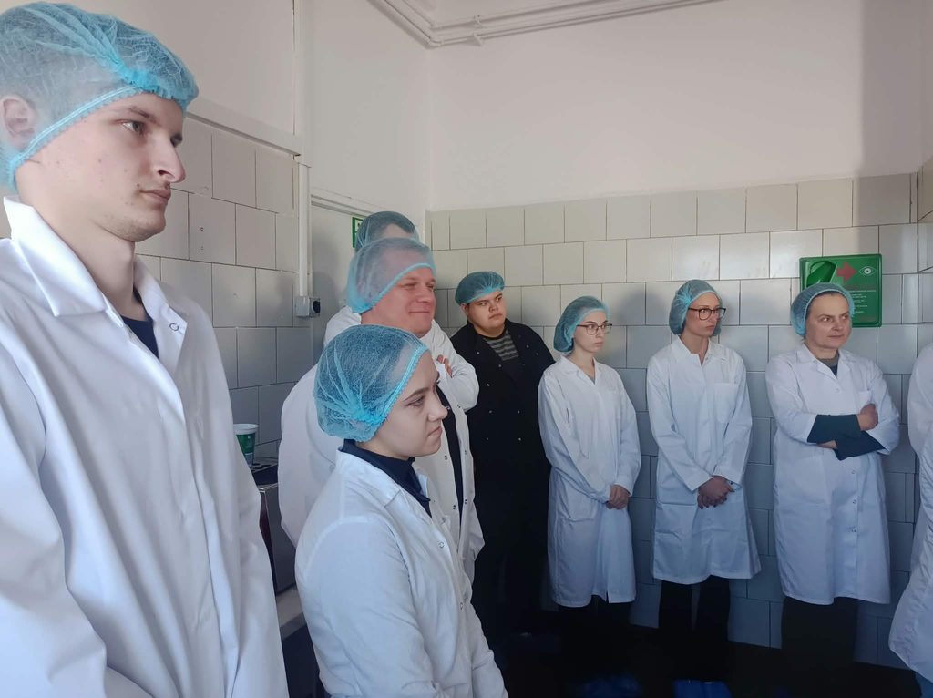 Studenci w strojach białych ochronnych w hali produkcyjnej wokół tło, ściany z białych płytek