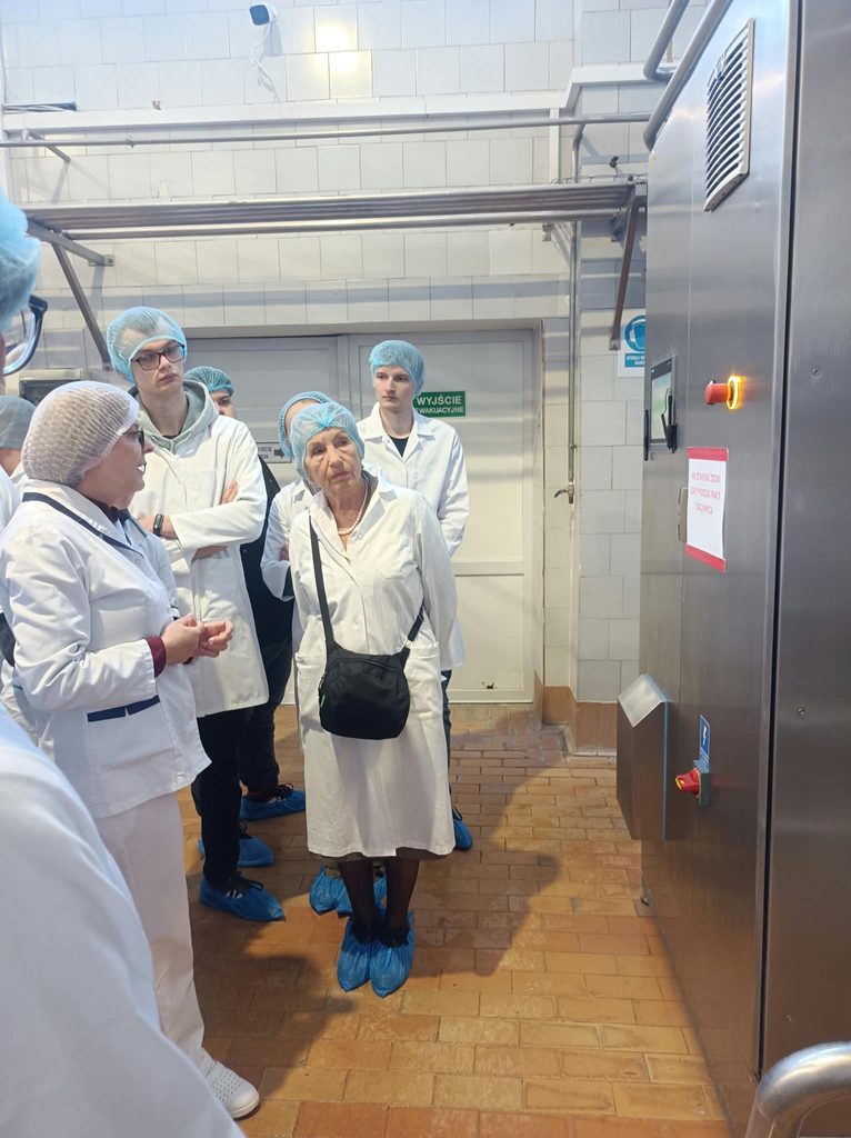 Studenci w strojach białych ochronnych w hali produkcyjnej obok urządzenia ze stali do produkcji i przetwórstwa mleka