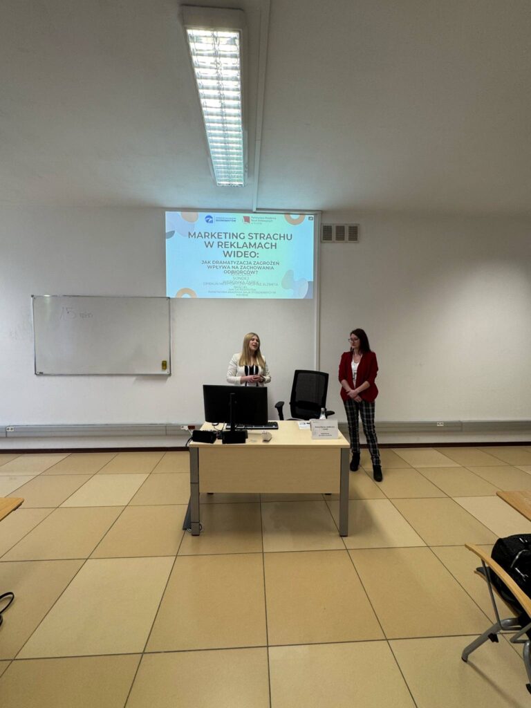 Studentki Karolina i Weronika podczas wystąpienia, biurko, prezentacja na ekranie