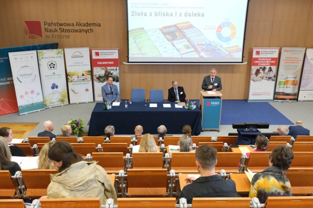 Widok auli, przód ekran, rolapy, stół komisji i przemawia Pan Kanclerz. Bliżej uczestnicy siedzą.