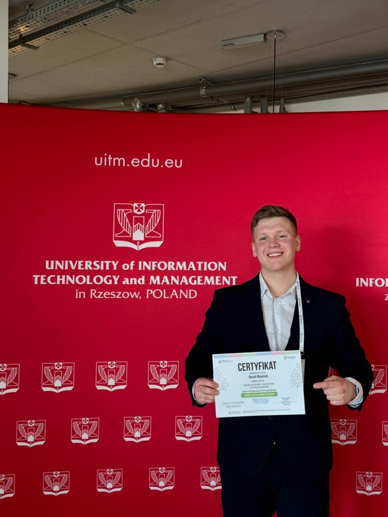 Student z certyfikatem na tle ścianki organizatora konferencji