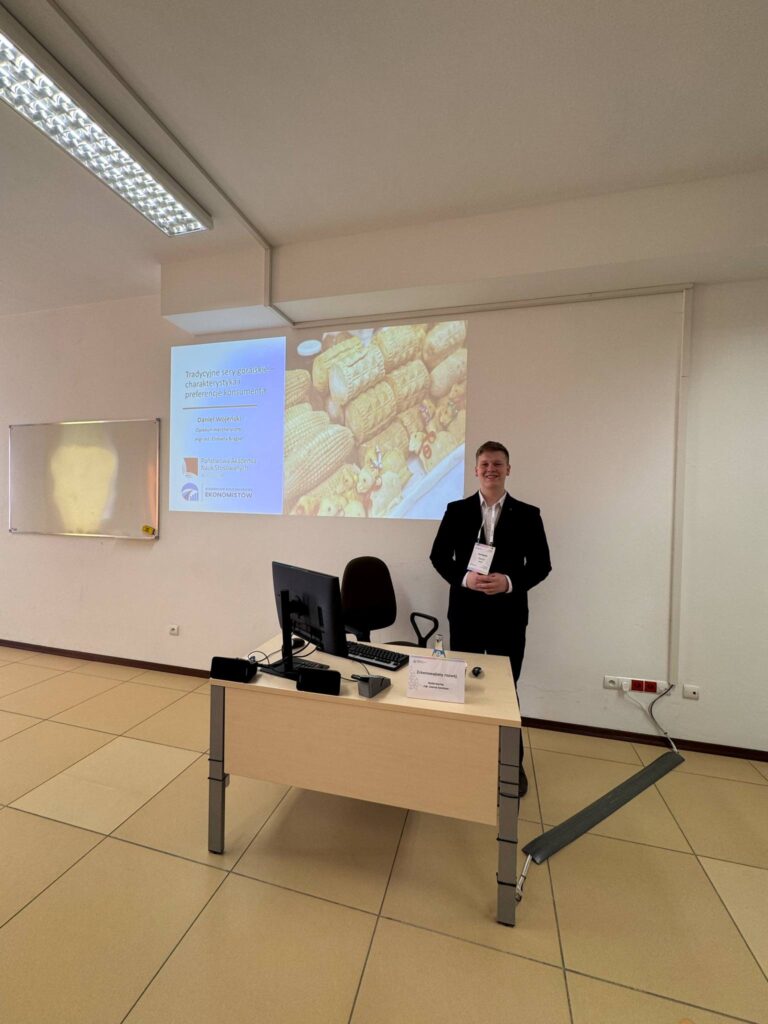 Student podczas wystąpienia na sali przy biurku, w tle prezentacja