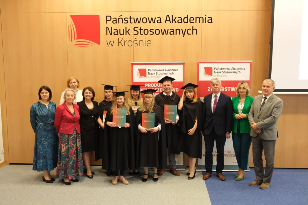 Wszyscy absolwenci z władzami i nauczycielami na tle baneru kierunku i logo uczelni
