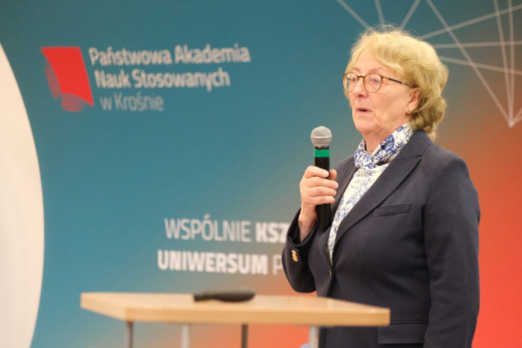 Na tle baneru uczelni przy mównicy z mikrofonem Pani Profesor Elżbieta Pisulewska