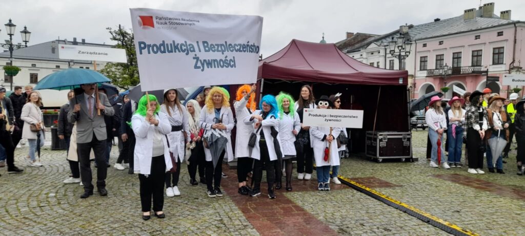 Studenci kierunku PIBŻ w kolorowych perukach i napisem kierunku stoją na pł
