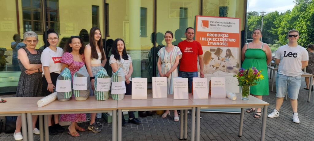 Grupa studentów za stołem z przygotowanymi z bańkach napojami i banerem kierunku