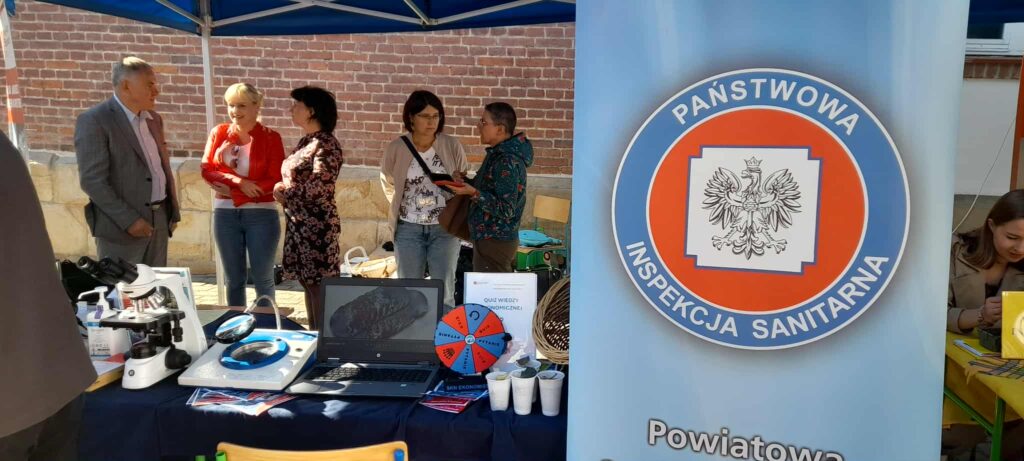 Rektor, dyrektor Sanepidu i kierownik zakładu oraz 2 pracowników, na pierwszym planie stoisko kierunki i baner Sanepidu