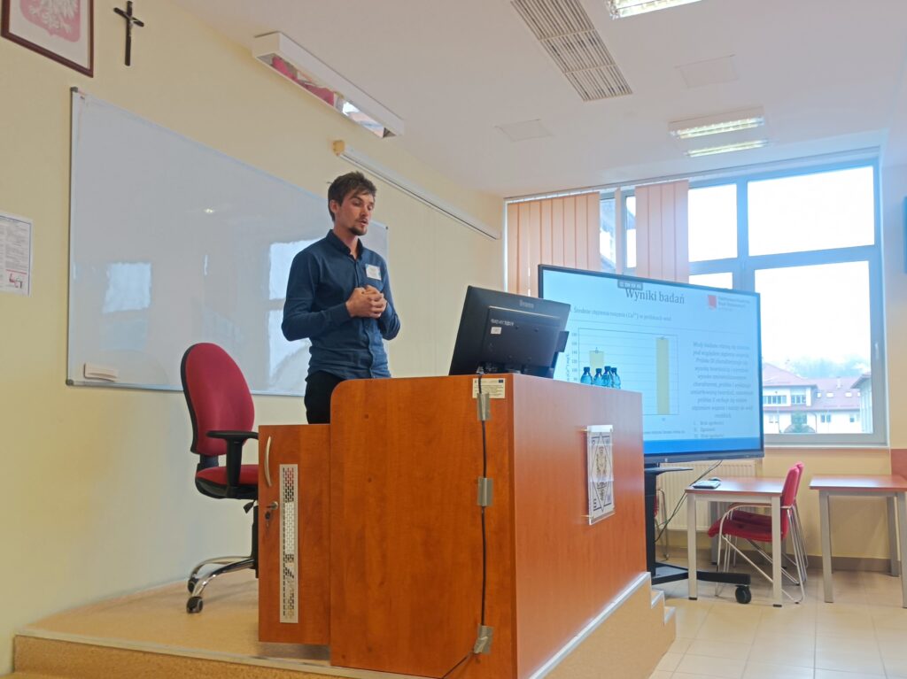 Student PIBŻ referuje swoje wystąpienie na podeście przy komputerze, za biurkiem