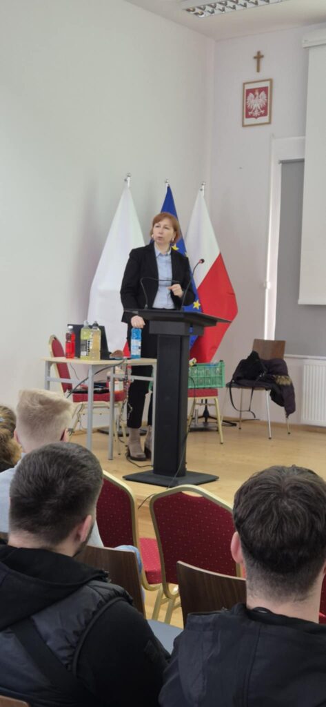 Scena, slajd z wykładem po prawej banery uczelni i kierunku, prowadząca głosi wykład pokazuje przykładowy produkt