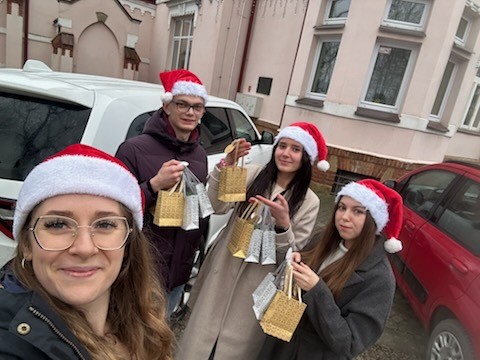 Studenci w czapeczkach mikołajowych i prezentami przed domem dziecka