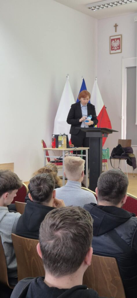 Scena, slajd z wykładem po prawej banery uczelni i kierunku, prowadząca głosi wykład pokazuje przykładowy produkt