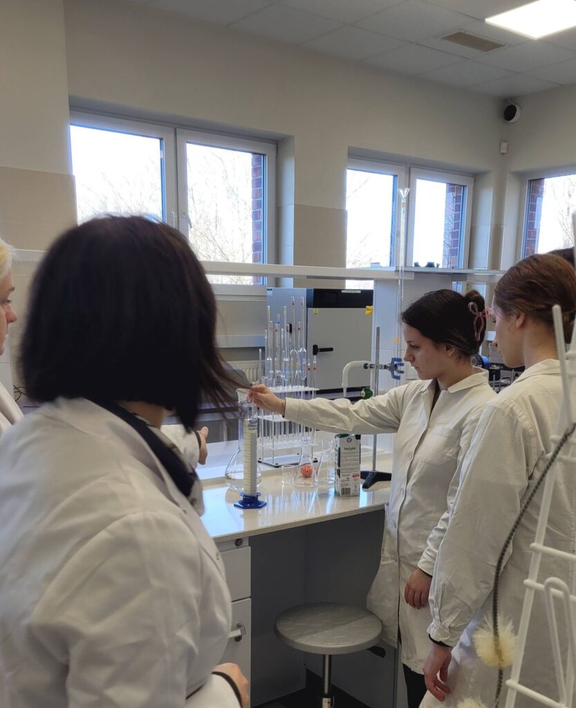 uczennica zanurza laktometr w cylindrze i bada mleko, obok prowadząca