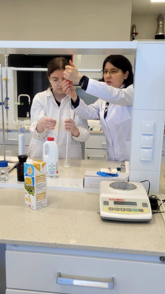 uczennica z pomocą prowadzącej pobiera pipetą próbkę mleka