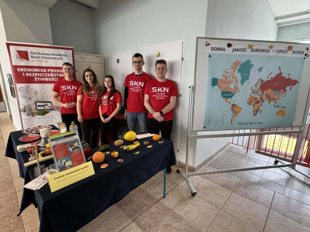 Studenci z kła SKN PIBŻ, baner za nimi, przed nimi stół z owocami, ulotkami, po prawej mapa polityczna świata