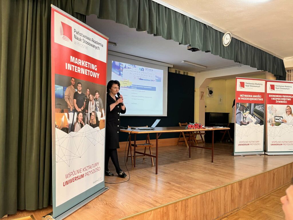 na scenie profesor Marczak wykłasza wykład z  boku banetr promocyjny , z tyłu ekran z prezentacją 