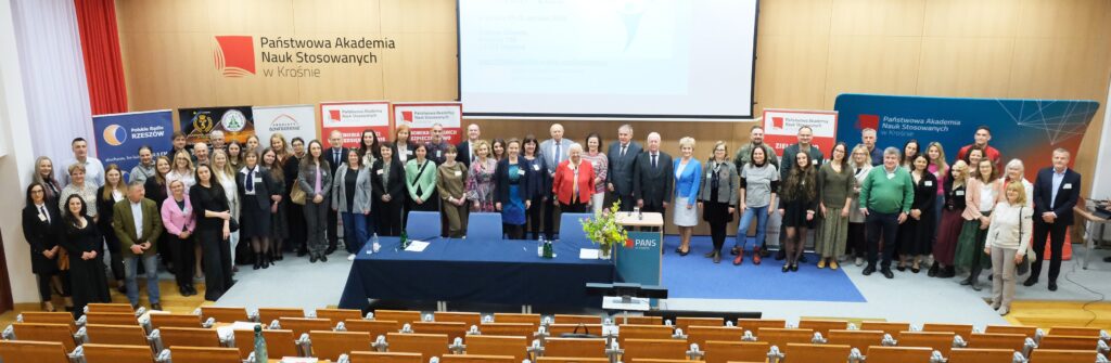 Wszyscy uczestnicy konferencji na tle sceny auli, logo uczelni i banerów kierunków i sponsorów