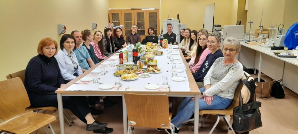 Studenci z nauczycielami siedzą przy stole zastawionym potrawami.