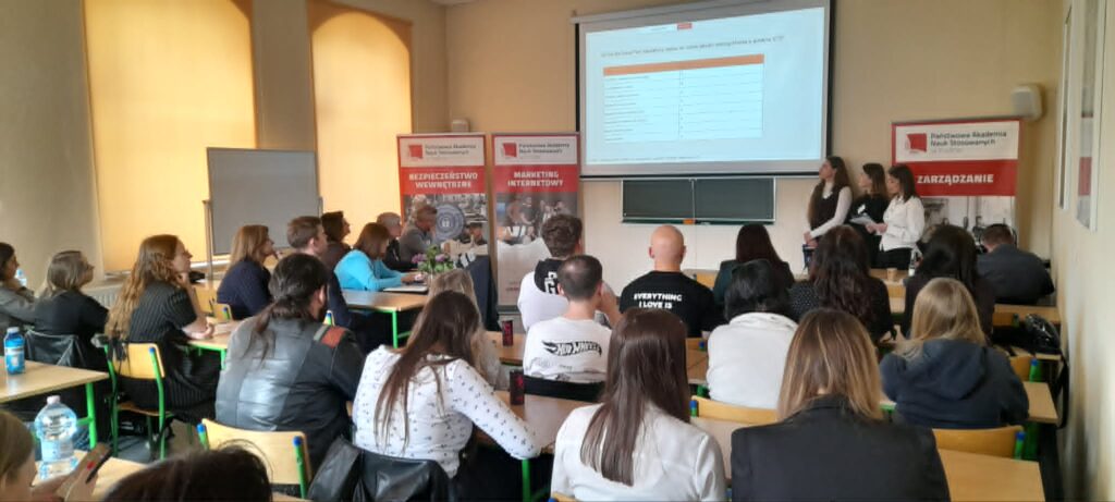 sala ze studentami biorącymi udział w konferencji ekran z prezentacją 3 studentów wygłasza swoje wystąpienie