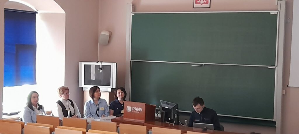 moderatorzy z jednego z paneli siedzą za stołem obrad w tle tablica i biurko