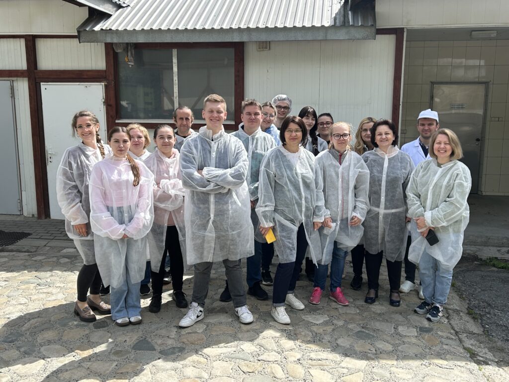 wszyscy studenci wyjazdu z opiekunami w odzieży ochronnej stoją na zewnątrz przez zakładem