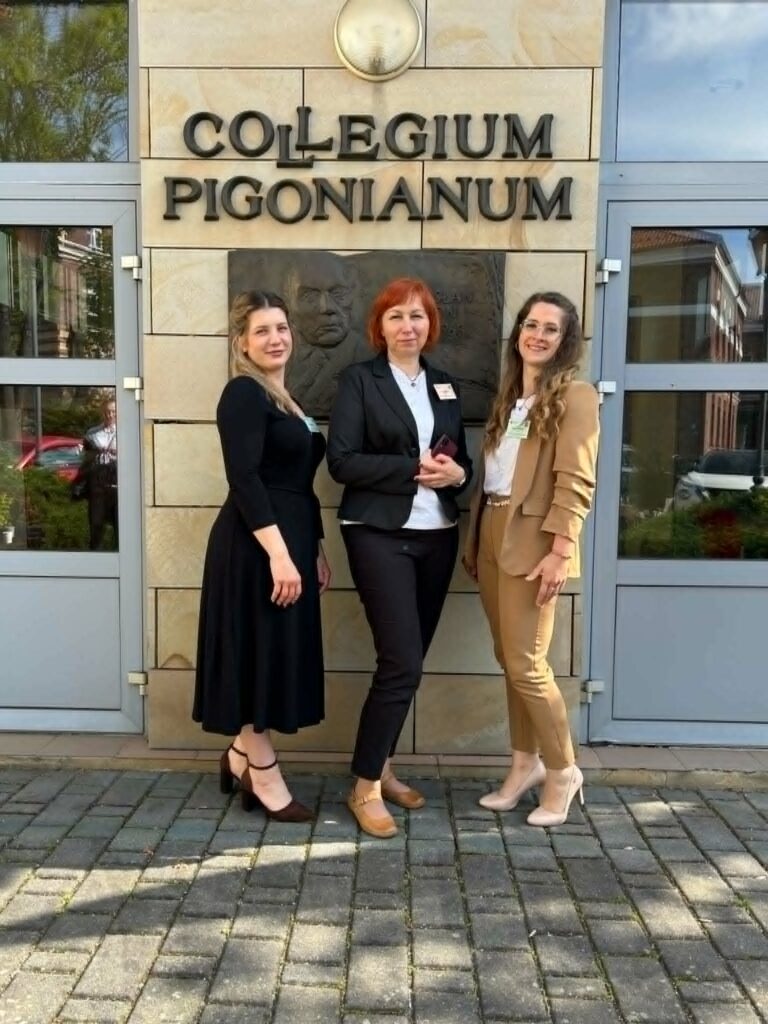 Katarzyna Bobek i Wiktoria Raś z opiekunem Elżbietą Brągiel stoją z certyfikatami na tle ściany z napisem Collegium Pigonianum