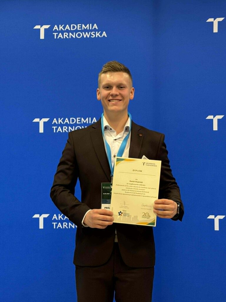Student stoi z dyplomem na tle ścianki Akademia Tarnowska